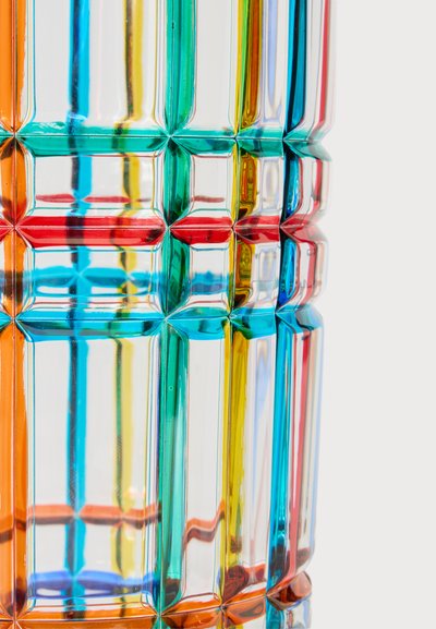 Gros plan de blocs de verre translucides et multicolores avec des lignes verticales et horizontales rouges, bleues, vertes, jaunes et oranges créant un motif géométrique.