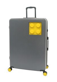 Gray hard shell suitcase with a yellow LEGO brick design on the front. Features a retractable handle and four yellow wheels.