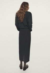 Donkergebreide trui met een losse pasvorm, gecombineerd met een lange, rechte zwarte rok met een split aan de achterkant; bruine schoenen en gestructureerde grijze sokken.