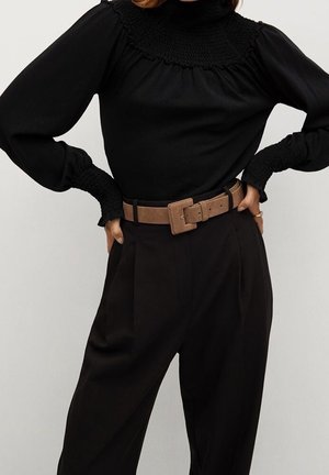 Schwarzes Oberteil mit hohem Kragen und gerafften Details, langen Ballonärmeln, kombiniert mit hoch taillierter schwarzer Hose und einem braunen Gürtel.