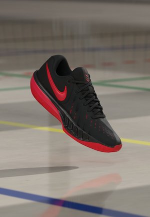 Black and red athletic shoe with Nike logo, floating above a gym floor marked with yellow, blue, green, and red lines.