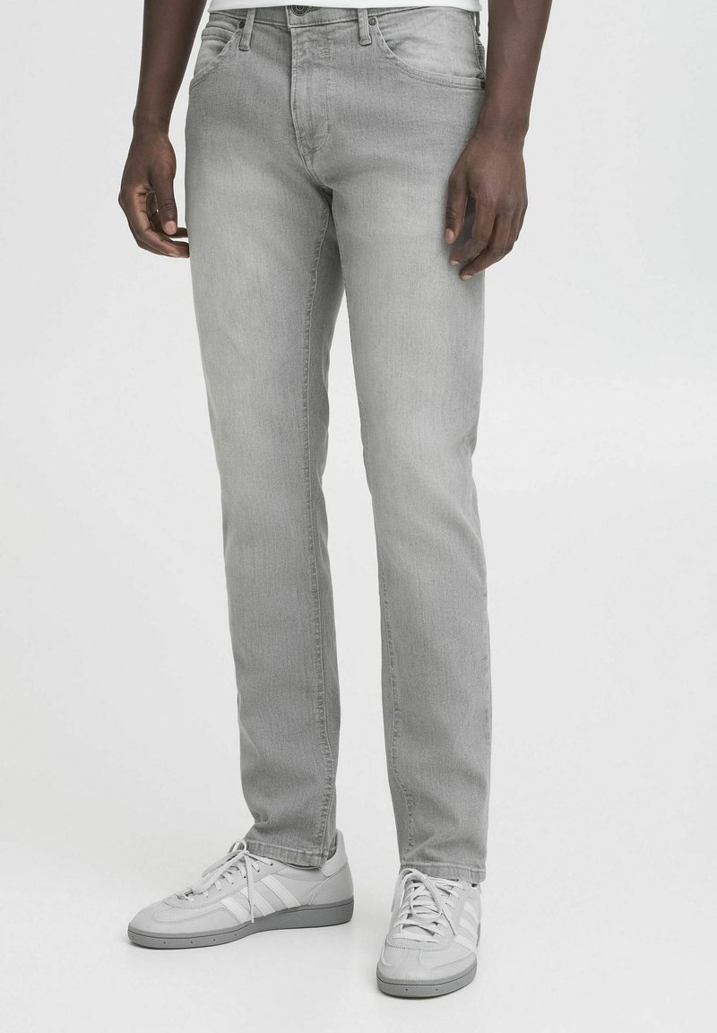 Jeans de mezclilla gris con corte recto, diseño de cinco bolsillos y un leve desvanecimiento. Combinados con zapatillas deportivas en gris claro.