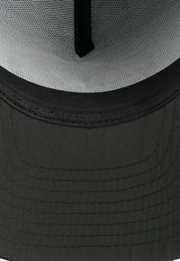 Casquette noire avec une visière plate et un tissu texturé. L'intérieur présente une doublure en mesh grise et des coutures noires le long de la visière.