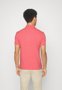 Polohemd mit kurzen Ärmeln in Koralle, aus einem weichen Textilgewebe gefertigt. Verfügt über einen klassischen Kragen und seitliche Schlitze für zusätzlichen Komfort.