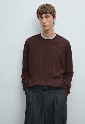 Långärmad, vinröd skjorta med grå rund hals, kombinerad med högmidjade, lösa svarta byxor. Slät textur, minimalistisk design.