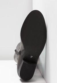 Botte en cuir noir avec une semelle texturée. Taille 37 marquée au fond. Présente un design élégant et une surface lisse.