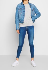 Giacca in denim azzurra, felpa grigia e jeans skinny neri. Sneakers bianche. La giacca presenta due tasche frontali e chiusura con bottoni.