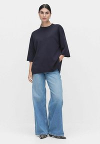 Marineblauw T-shirt met korte mouwen en een ronde hals, met zijzakken, gecombineerd met lichtblauwe hooggerokte flared jeans en gemusterde zwarte schoenen.