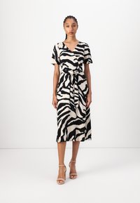 Svart og kremfarget zebra-stripete kjole med omslagdesign, korte ermer og knyttet midje, laget av et glatt stoff. Sko: naken strappy hæler.