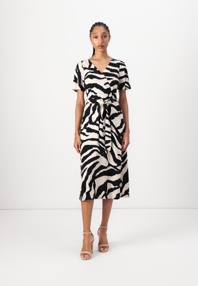 Svart og kremfarget zebra-stripete kjole med omslagdesign, korte ermer og knyttet midje, laget av et glatt stoff. Sko: naken strappy hæler.