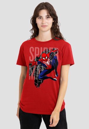 Young woman wearing a red t-shirt with a Spider-Man graphic and web design, standing against a plain light gray background.
