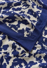 Tissu plié avec un motif abstrait irrégulier bleu marine et blanc, montrant une texture en couches et des détails de tissage doux.