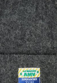 Tumehall villane kootud kangas, millele on õmmeldud värvikas silt "LA MAISON AMV SUPERVINTAGE".