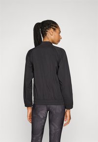 Black lightweight jacket with a ribbed hem, long sleeves, and a stand-up collar. Worn over dark patterned leggings.