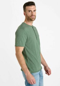 Green short-sleeve shirt with a henley neckline, featuring three buttons. Made of soft fabric, with a relaxed fit and smooth texture.
