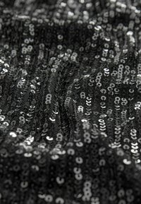Tissu noir recouvert de sequins argentés brillants, avec une surface texturée au design ondulé, reflétant la lumière dans différentes directions.