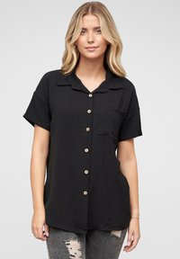 Camicia nera a maniche corte con tessuto strutturato e taschino sul petto. Presenta bottoni di legno e una vestibilità comoda.