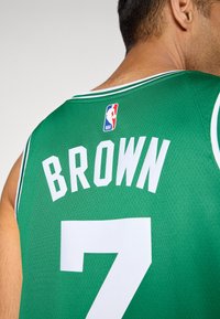 Mand, der bærer en grøn NBA basketballtrøje med navnet "BROWN" og nummer 7 synligt på ryggen.