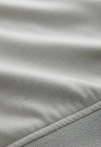 Gaiši pelēks audums ar gludu tekstūru, ar vieglu ribiņu un smalku spīdumu. Malā redzama plakana šuvju šuve, kas nodrošina izturību.