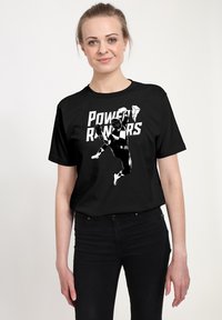 Černé bavlněné tričko s bílou grafikou skáčící postavy a textem "Power Rangers" v tučných písmenech nahoře.