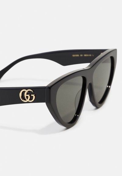 Black cat-eye sunglasses made of glossy plastic; features dark lenses and gold GG logo on the side. Sleek, modern design with pronounced angles.