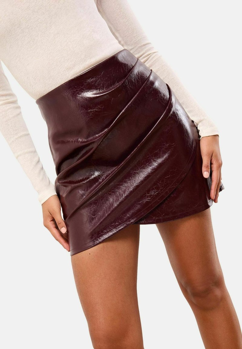 Burgundi műbőr mini szoknya, drapéria kialakítással, fényes felülettel és aszimmetrikus szegéllyel.