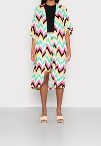 Kleurrijk kimono met chevronpatroon in mintgroen, roze, zwart en geel, gecombineerd met een zwart crop top en bijpassende shorts met patroon.