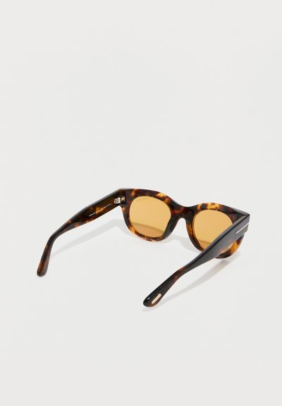 Γυαλιά ηλίου με σκελετό από κελύφη χελωνών και φακούς με κεχριμπαρένιο χρώμα, ακουμπισμένα σε λευκή επιφάνεια, γωνιασμένα για να εμφανίζουν το μπροστινό μέρος και τα πλαϊνά μπράτσα.