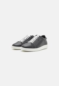 Sneaker in pelle nera con finitura liscia, lacci bianchi e suola in gomma bianca. Presenta un design laterale discreto e una linguetta sul retro.