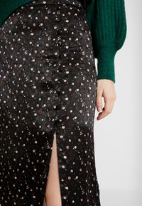 Černá květinová sukně s drobnými růžovými a bílými květy, předním rozparkem a knoflíkovým zdobením po straně. Texturovaná látka.