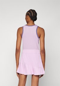 Top sin mangas morado con textura de malla, combinado con una falda plisada morada clara que presenta un diseño asimétrico en el dobladillo.