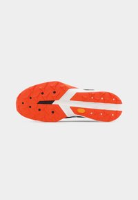 Φωτεινή πορτοκαλί και λευκή σόλα αθλητικού παπουτσιού με υφή πρόσκρουσης και μικρές μαύρες κυκλικές ένθετες, πάνω σε απλό ανοιχτό φόντο.