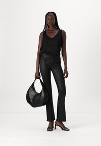 Black sleeveless top, fitted black flared pants, and open-toe black heeled sandals. Holding a black leather hobo bag with curved design.