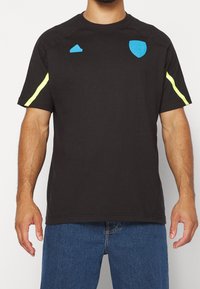 Černé sportovní tričko s krátkým rukávem a kulatým výstřihem, zdobené modrými logy a fluorescenčními žlutými pruhy na ramenou.