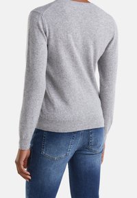 Šedý pletený svetr s kulatým výstřihem, dlouhými rukávy, žebrovaným lemem a hladkou texturou, který je zkombinován s tmavě modrými džíny.