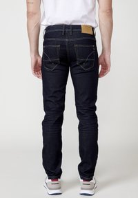 Dunkelblaue Denim-Jeans mit Slim-Fit, ausgestattet mit gelber Ziernaht, zwei Gesäßtaschen und einem tannfarbenen Lederlogo-Patch am Bund.