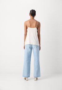 Top sin mangas de color crema con tirantes finos, combinado con jeans de pierna ancha de color azul claro. La modelo está de espaldas al espectador.
