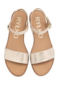 Złote metaliczne płaskie sandały z dwoma szerokimi paskami, wąskim paskiem na kostce i klamrą. Brązowa wkładka z wytłoczonym białym logo marki.