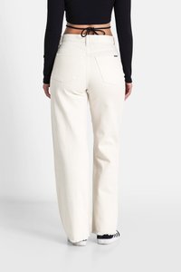 Jeans in denim bianco a gamba larga con orlo sfrangiato, due tasche posteriori e vita alta, abbinati a un top aderente nero a coste.