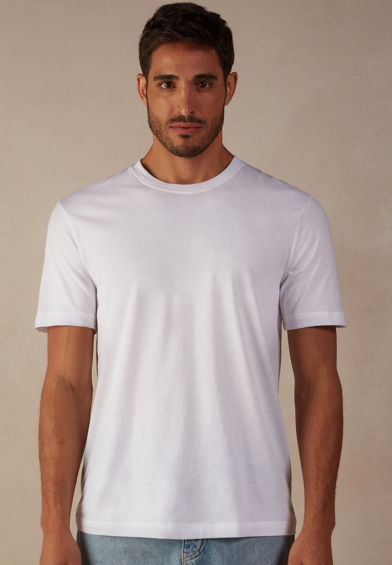 T-shirt en coton blanc à manches courtes avec un col rond ; texture lisse ; coupe classique. Aucun motif ni accent visible.