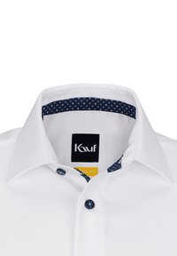 Weißes Hemd mit Knöpfen und strukturierter Kragen und einem dunkelblau gemusterten Innenfutter. Hergestellt aus einem strukturierten Stoff und blauen Knöpfen.