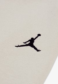 Bežna tkanina s teksturiranim završetkom ima crni Jumpman logo izvezene na površini, postavljen s desne strane.