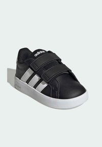 Černá obuv z umělé kůže s bílými akcenty a třemi horizontálními pruhy. Má suché zipy a bílou gumovou podrážku.