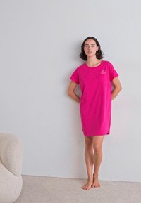 Rosa bomullskjole med kortermede, en frontlomme og en avslappet passform. Glatt tekstur, knelengde med sidesømmer.