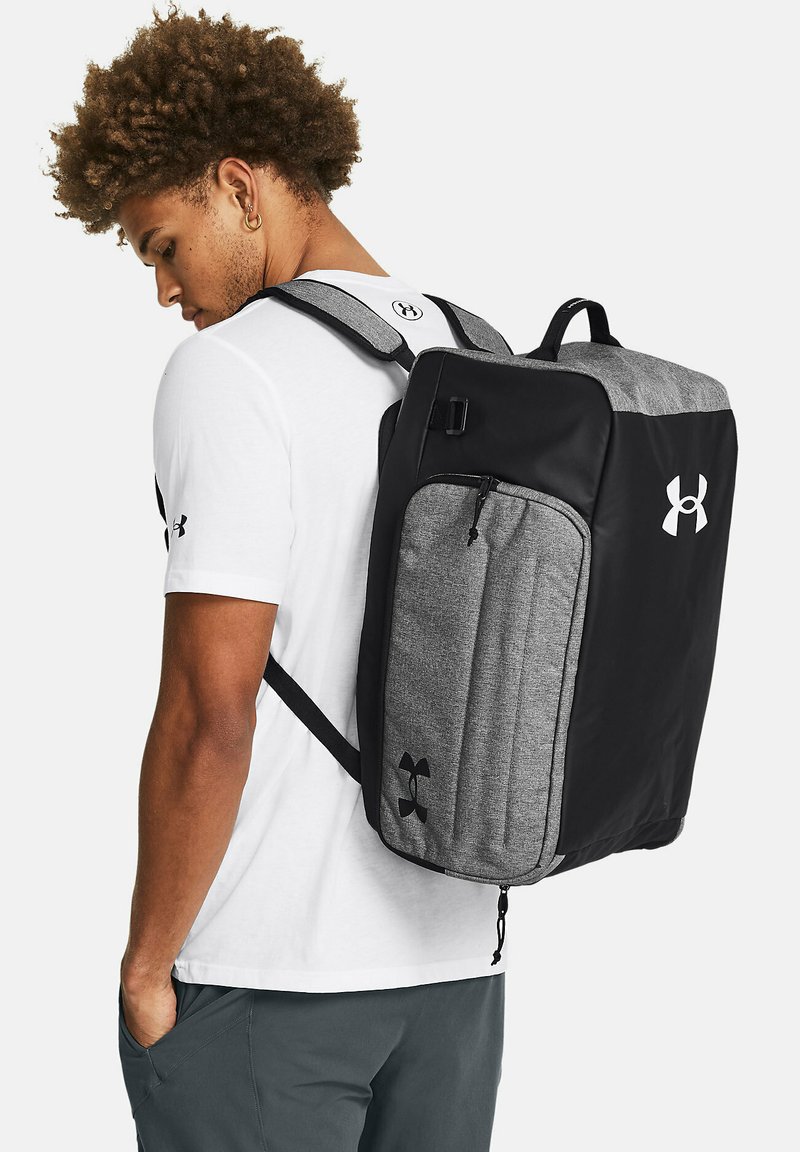 Zaino nero e grigio con design rettangolare, realizzato in tessuto. Presenta spallacci regolabili e una tasca frontale con cerniera. Logo mostrato in modo prominente.