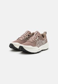 Ute løpesko i lys brun mesh med hvite detaljer, teksturert såle og polstret krage. Har asics-logo og flate lisser.
