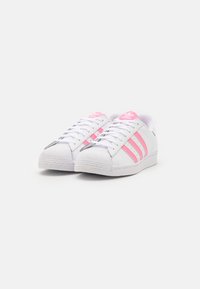 White Adidas sneakers with pink stripes and logos, placed side by side on a plain white background.