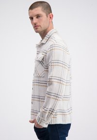 Geweven flanellen overhemd in het wit met een ruitpatroon in grijs en mosterdgeel. Voorzien van een knoopsluiting aan de voorkant, kraag en borstzak. Gecapitonneerde stof.