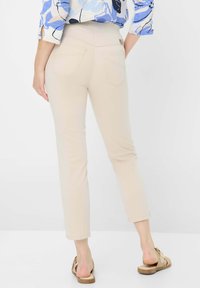 Beige enkelhoge broek met een slim fit, voorzien van achterzakken en een gladde textuur. Gekocht met een gestreept blauw-wit bovenstuk.