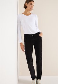 Witte lange mouwen top met een V-hals, gecombineerd met zwarte slim-fit broek. Zwarte broek heeft zijzakken en een knoopsluiting.